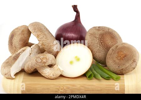 Shiitake-Pilze und verschiedene Zwiebelsorten auf einem Holzschneidbrett auf weißem Hintergrund. Rezepte und Heilkräuter Stockfoto