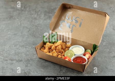 Pappbox mit leckerem gebratenem Popcorn-Hähnchen auf grauem Hintergrund, serviert mit Sauce und Mayonaise. „On the Go“-Konzept Stockfoto