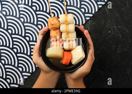 Eine Schale mit japanischer Fischkugel-Suppenspieße, von weiblicher Hand gehalten, Draufsicht Stockfoto