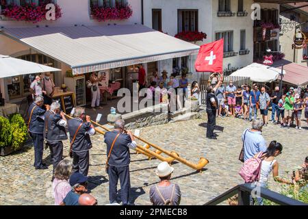 Gruyere, Schweiz - Juli 29,2021: Eine Schweizer Musikergruppe spielt das traditionelle Musikinstrument Alphorn mit einem Fahnenträger, um die National Fla zu schwingen Stockfoto