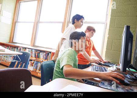 Die Verwendung von Computern bereits in jungen Jahren hat mehrere Vorteile. Grundkinder, die in der Schule an Computern arbeiten. Stockfoto