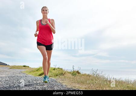 Der Gesundheit und dem Wohlbefinden gewidmet. Eine junge Frau, die am Meer joggt. Stockfoto