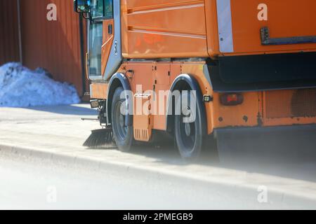 Orangefarbene Straßenkehrmaschine reinigt den Bürgersteig an einem Frühlingstag. Stockfoto