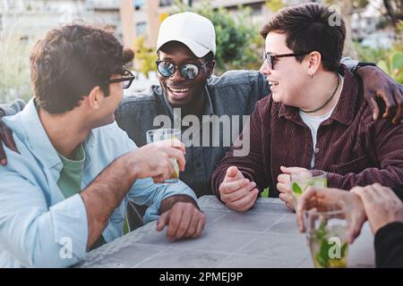 Eine Gruppe junger Freunde, darunter ein weißer Mann, eine nicht-binäre, übergroße Person mit kurzen Haaren und Nasenlöchern, und eine afrikanische Person, die sich unterhält Stockfoto