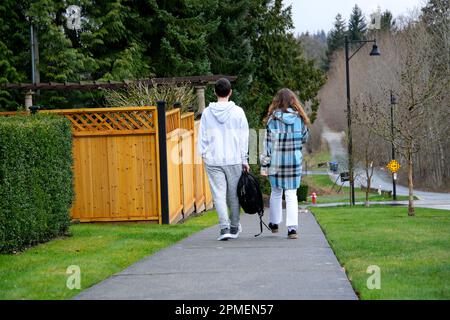 Im privaten Sektor gehen zwei Schulleute mit dem Rücken auf dem Bürgersteig auf dem Bürgersteig entlang zum privaten Fotosektor Teenager und Mädchen zurück in die Schule Stockfoto