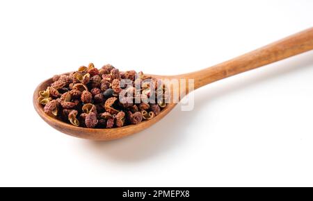 Sichuanpfeffer und Holzlöffel auf weißem Hintergrund. Sichuan Pfeffer ist ein Mitglied der Familie Sansho, die in der chinesischen Küche verwendet wird. Stockfoto