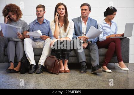 Sitzen und warten. Foto einer Gruppe von Geschäftsleuten, die in einer Reihe auf dem Sofa sitzen. Stockfoto