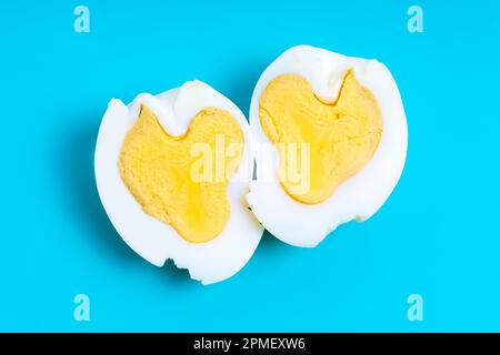 Zwei herzförmige Hälften eines gekochten Eies, isoliert auf blauem Hintergrund. Kreatives Gesundheits- und ernährungsbezogenes Konzept. Stockfoto