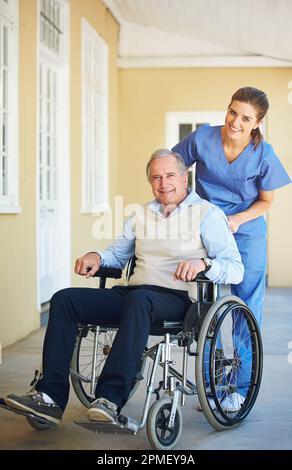 Sie kümmern sich hier so gut um mich. Eine Ärztin schubst ihre ältere Patientin im Rollstuhl. Stockfoto