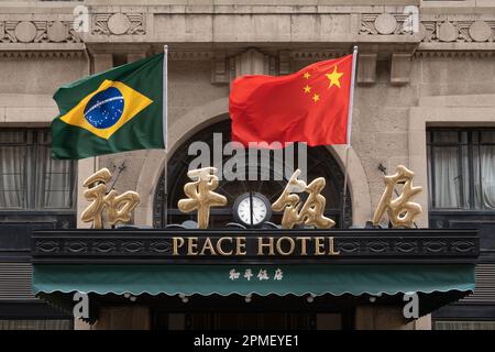 SHANGHAI, CHINA - 13. APRIL 2023 - Chinesische und brasilianische Nationalflaggen flattern im Wind über dem Haupteingang des Peace Hotels an der Nanjing Road Stockfoto