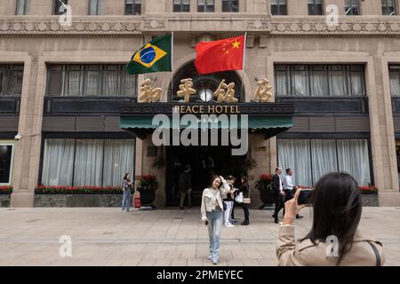 SHANGHAI, CHINA - 13. APRIL 2023 - Chinesische und brasilianische Nationalflaggen flattern im Wind über dem Haupteingang des Peace Hotels an der Nanjing Road Stockfoto