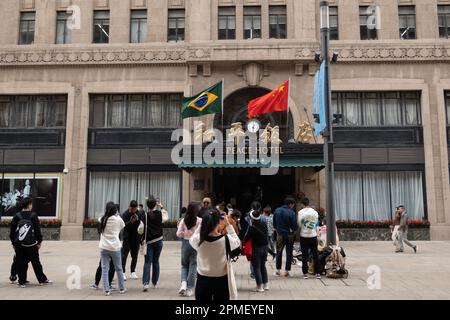 SHANGHAI, CHINA - 13. APRIL 2023 - Chinesische und brasilianische Nationalflaggen flattern im Wind über dem Haupteingang des Peace Hotels an der Nanjing Road Stockfoto
