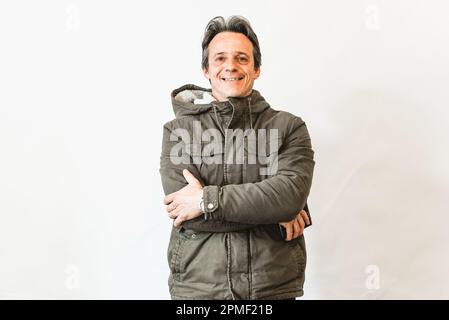 Fröhlicher, lachender Mann, lächelnder alter alter alter Herr, trägt eine grüne Jacke, die Arme gekreuzt, isoliert auf einer weißen Wand, Porträt Stockfoto