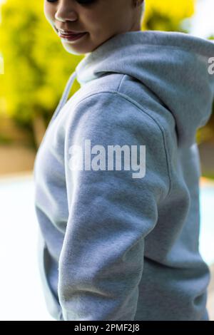 Nahaufnahme einer glücklichen, birassischen Frau, die einen grauen Hoodie über dem Swimmingpool im Garten trägt Stockfoto