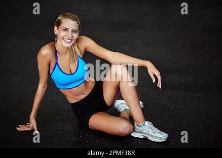 Mach deinen Körper zu dem sexiesten Outfit, das du besitzt. Eine sportliche junge Frau, die drinnen sitzt. Stockfoto