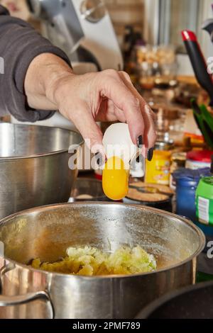Der Koch knackt ein Ei in ein Gericht, das in einer Schüssel zubereitet wird. Stockfoto