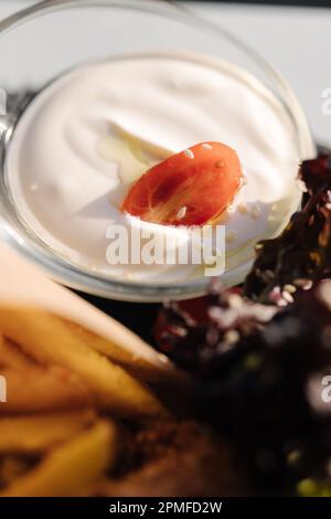 Leckere weiße Sauce auf Basis von Sauerrahm und Mayonnaise mit Tomatenscheibe. Pommes frites Stockfoto