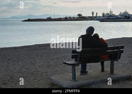 Ein junges Paar sitzt im Frühling und beobachtet den Sonnenuntergang über dem Yachthafen Glyfada am Stadtrand von Athen Stockfoto