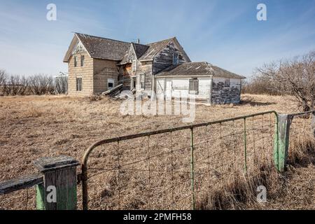 Ein traditionelles ländliches Wohnhaus mit weißem Lattenzaun und Pfosten, das sich in einem Feld mit hohem Gras und Wildblumen befindet Stockfoto