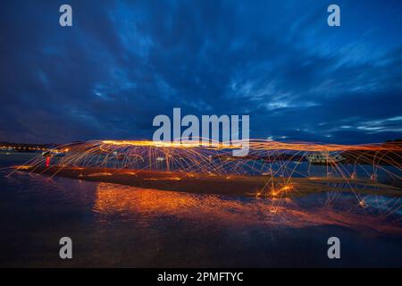 Reflexion von Funkenfeuer aus Stahlwolle mit langlebigen Geschwindigkeits-Bewegungen abstrakt bei Sonnenaufgang im Meer. Lichtfunken prallen vom Wasser ab Stockfoto