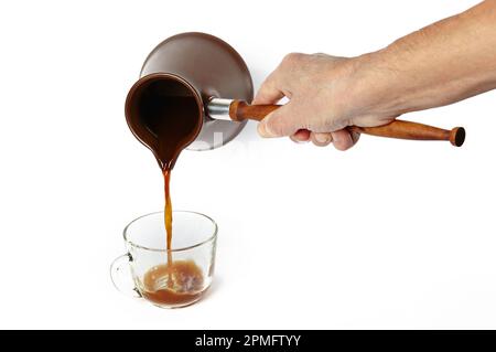 Mann, der Kaffee in eine Tasse gießt, isolierter weißer Hintergrund. Clay Cezve für die Kaffeezubereitung in der Hand Stockfoto