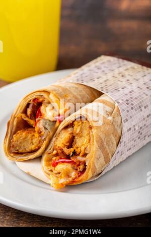 Hähnchenwicklung mit Gemüse auf einer weißen Porzellanplatte auf einem Holztisch Stockfoto