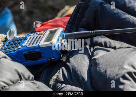 Nahaufnahme eines gebrauchten Walkie-Talkie-Radios mit Tastatur über warmer Kleidung an einem sonnigen Wintertag. Abenteuer, Erkundungskonzept Stockfoto