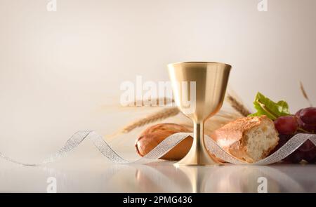 Kelch auf weißem Tisch mit Brot und Trauben dahinter mit weißem isoliertem Hintergrund. Vorderansicht. Stockfoto