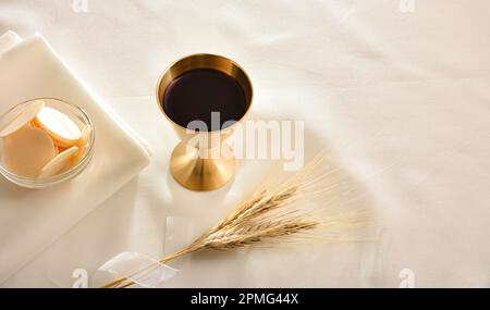 Kelchbecher mit Wein und geweihten Wirten in einem Behälter auf weißer Tischdecke und Weizenspikes. Erhöhte Aussicht. Stockfoto