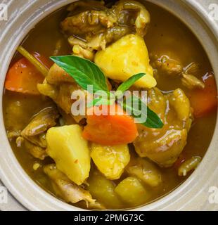 Gedünstetes Hähnchen mit Kartoffeln und Gemüse auf blauem Teller isoliert auf schwarzem Hintergrund, Draufsicht Stockfoto