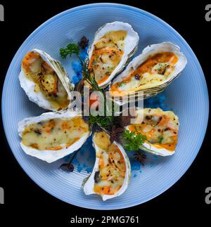 Austern, gebacken mit Käse auf einem Teller mit blauem Salz, isoliert auf schwarzer Draufsicht Stockfoto