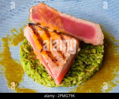 Thunfischsteak Medium, selten serviert mit Erbsen, isoliert auf schwarzem Hintergrund, Seitenansicht Stockfoto