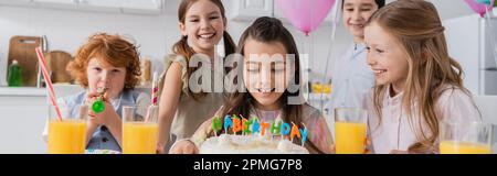Fröhliches Mädchen, das sich Geburtstagskuchen in der Nähe glücklicher Freunde anschaut, während der Party zu Hause, Banner, Stock Image Stockfoto