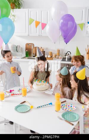 Gruppe glücklicher Kinder in Partymützen, die Spaß beim Geburtstag zu Hause haben, Stock Image Stockfoto