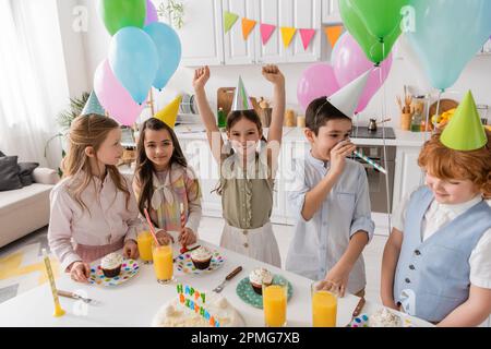 Gruppe und glückliche Kinder in Party Caps haben Spaß während des Geburtstags zu Hause, Stock Image Stockfoto