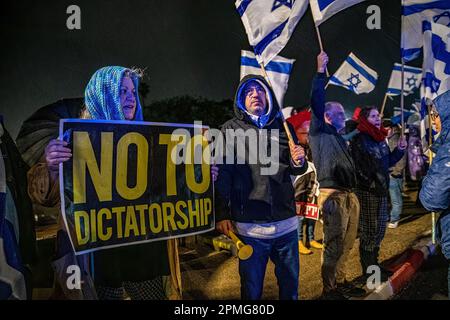 Hadera, Israel. 12. April 2023. Reformfeindliche Demonstranten schwenken israelische Flaggen und halten während der Demonstration Schilder im Regen. Demonstranten für und gegen die Justizreform in Hadera demonstrieren vor einer Mimouna-Zeremonie unter Teilnahme von Ministerpräsident Benjamin Netanjahu, dass es Konfrontationen zwischen reformfeindlichen Demonstranten und reformfreundlichen rechtsgerichteten Aktivisten gab. Kredit: SOPA Images Limited/Alamy Live News Stockfoto