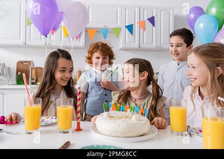 Gruppe glücklicher Kinder, die Geburtstag feiern, neben leckerem Kuchen während der Party zu Hause, Stockbild Stockfoto