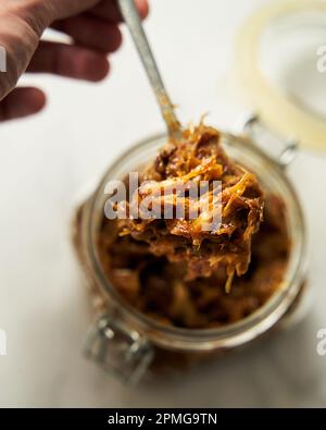Hausgemachte karamellisierte Zwiebeln im Glas. Die Hand des Mannes mit dem Löffel reicht in das Glas Stockfoto