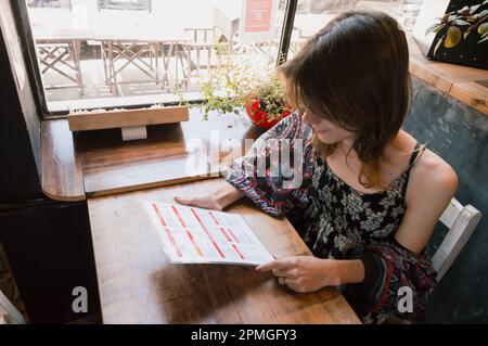 transsexuelle argentinische ethnische Zugehörigkeit junge lateinische Frau, die im Restaurant Entscheidungen trifft, die Speisekarte liest, am Tisch sitzt, Geschäftskonzept, Kopierbereich. Stockfoto