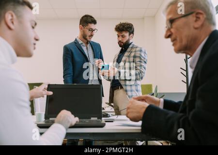 Ein intelligenter exzentrischer Geschäftsmann zeigt seinem Partner den Hintergrund für seine neue Social-Media-Plattform im Entwicklungsbereich des Büros Stockfoto