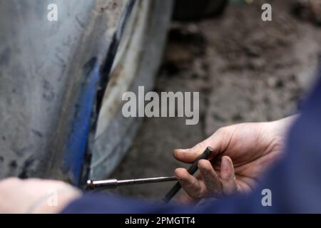 Männliche Hand repariert altes Auto. Automechaniker bei der Arbeit am Automotor in der Mechanikwerkstatt. Kfz-Mechaniker, der in der Garage arbeitet. Reparaturservice. Schmutzige Hände Stockfoto