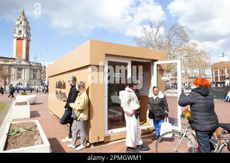 London, UK, 13. April 2023: Am Windrush Square, Brixton, ist ein riesiger Schuhkarton eingetroffen, der eine Pop-up-Ausstellung „Walk a Mile in My Shoes“ am Empathy Museum zeigt. Besucher wählen ein Paar Schuhe und hören sich eine Aufzeichnung des Schuhbesitzers an, in der sie über ihre Erfahrungen mit dem Brixton-Aufstand von 1981 oder anderen Aufständen in Bristol und Liverpool in dieser Zeit sprechen. Anna Watson/Alamy Live News Stockfoto