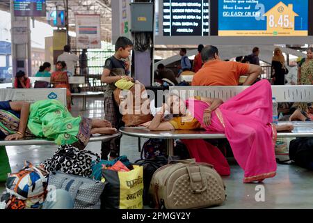 Eine Sari-bekleidete Zugfahrerin am Chhatrapati Shivaji Maharaj Terminus in Mumbai, Indien, entspannt sich auf einer Bank, während sie auf ihren Zug wartet Stockfoto