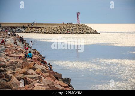 Eine Gruppe junger Menschen fischen an einem Wellenbrecher im Hafen von Pirapolis, während andere im Hintergrund laufen Stockfoto