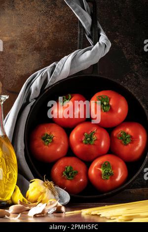 Frische Tomaten in der Pfanne und natives Olivenöl extra auf dunklem Hintergrund Stockfoto