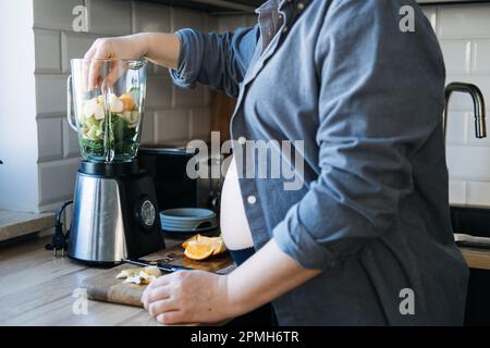 Smoothies und Nahrungsmittel gegen Schwangerschaftsurbelkeit. Anti-Ubelkeit-Morgenkrankheit-Smoothie. Schwangere Frau bereitet grünen VitaminSmoothie aus verschiedenen Früchten zu Stockfoto