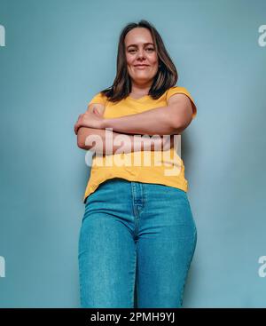 Eine junge Frau aus dem unteren Winkel kreuzte die Arme auf blauem Hintergrund Stockfoto