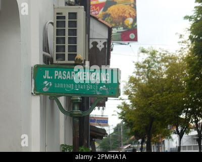Ein grünes Schild, das Straßennamen in Yogyakarta mit Bäumen und alten Gebäuden im Hintergrund anzeigt. Stockfoto