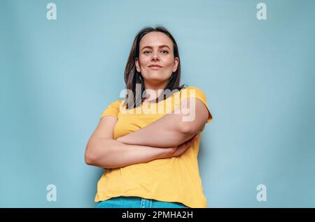 Eine junge Frau aus dem unteren Winkel kreuzte die Arme auf blauem Hintergrund Stockfoto