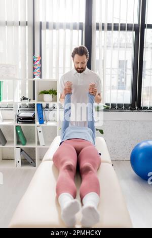 Bärtige manuelle Therapeutin streckt Arme der Frau während der Genesungsmanipulation in einem modernen Rehabilitationszentrum, Stockbild Stockfoto